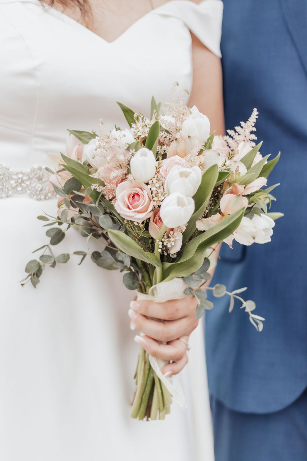 A delicate bridal bouquet with pink roses, white flowers, and eucalyptus leaves tied with ribbon.