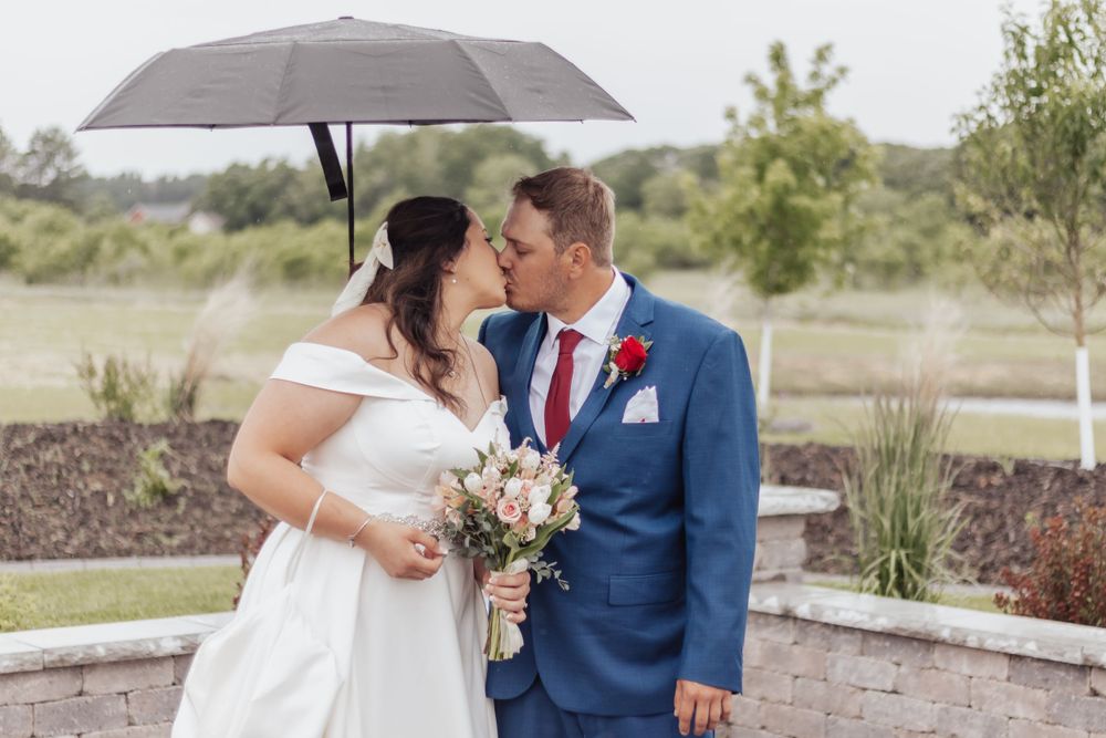 A couple shares an intimate moment under an umbrella in a garden setting during their wedding celebration.