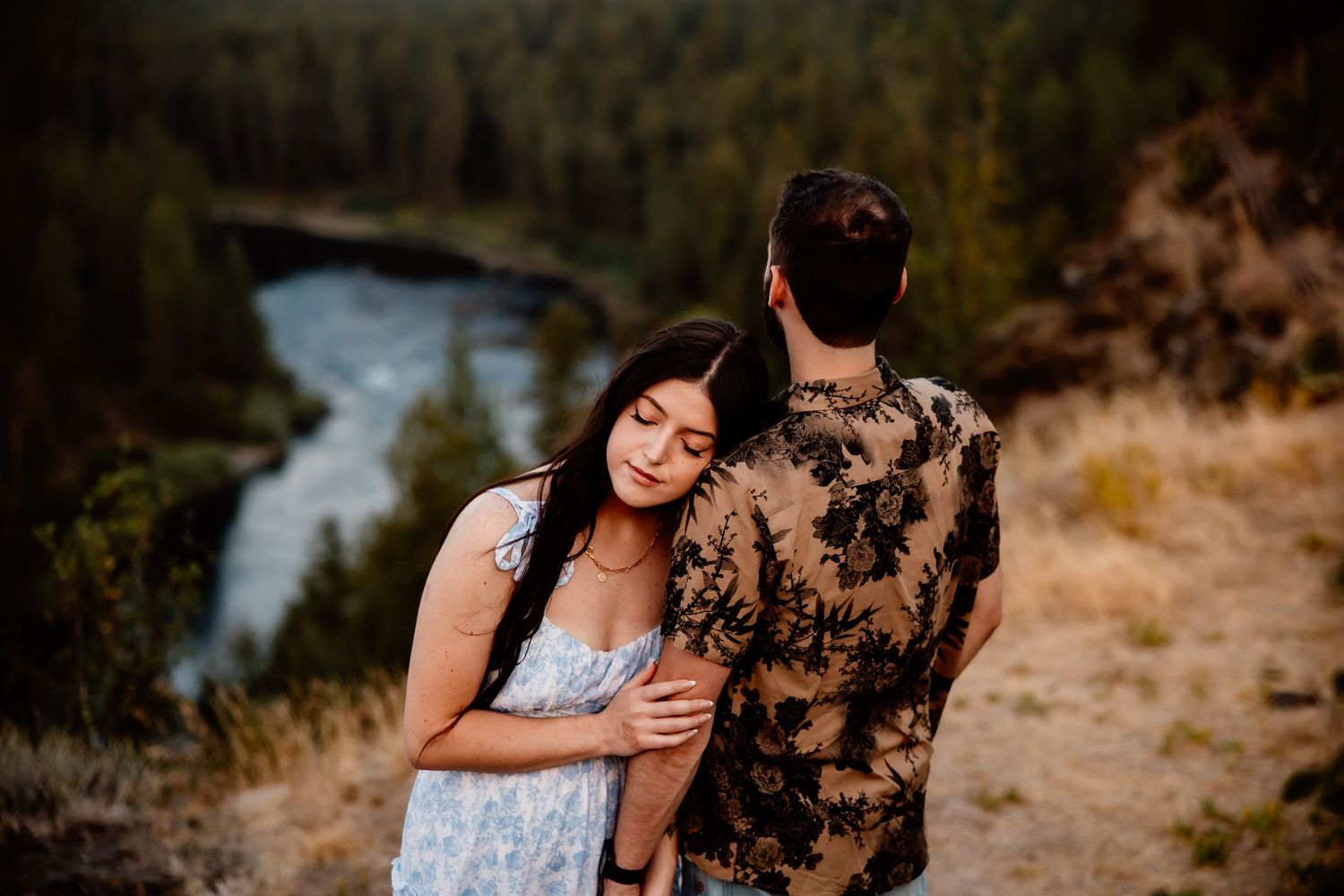 Romantic photoshoot at sunset overlooking a winding river from a clifftop viewpoint.