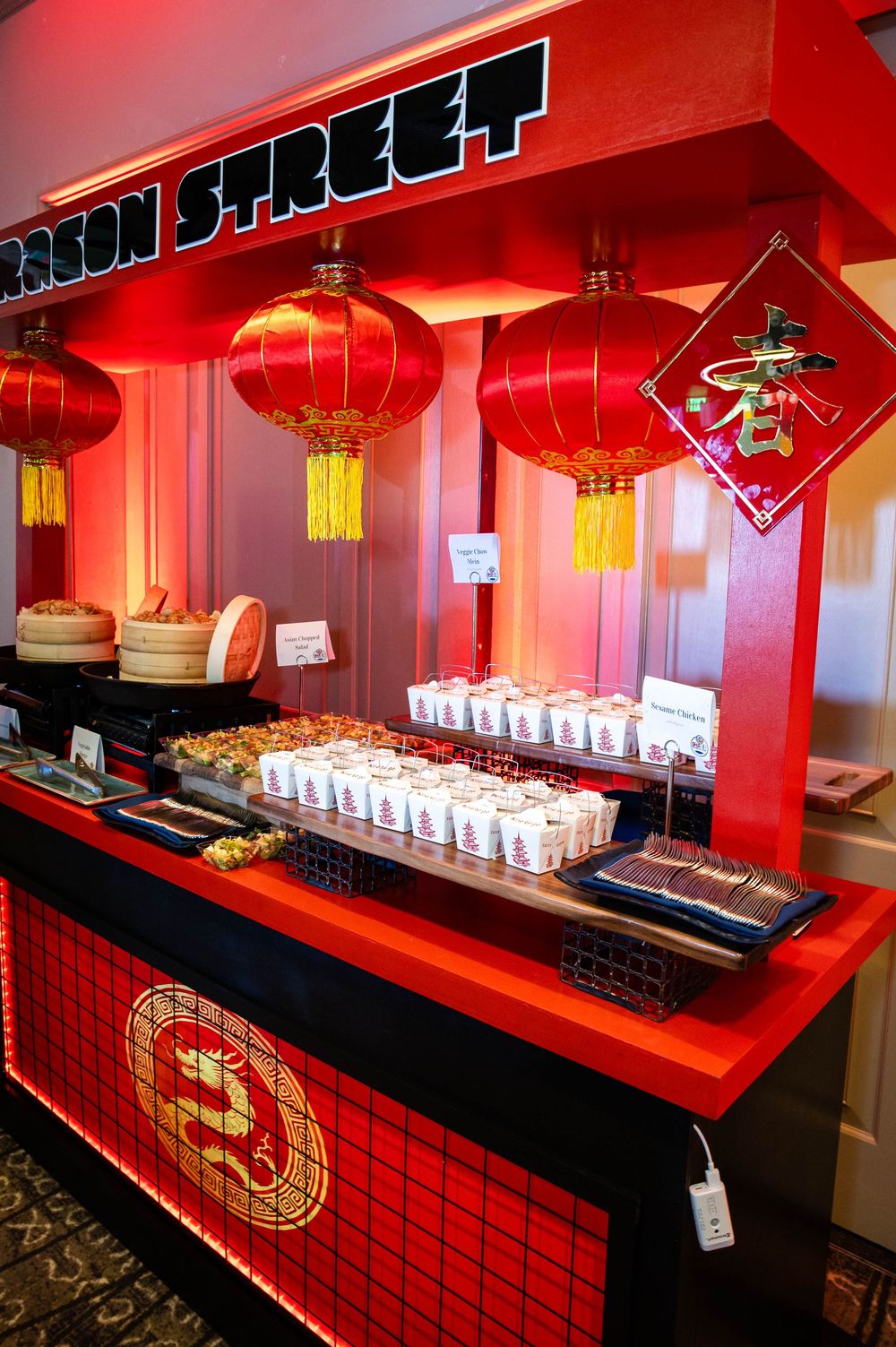 Red Chinese-themed Dragon Street food station with paper lanterns, steamer baskets, and takeout boxes lined up on a lit counter.