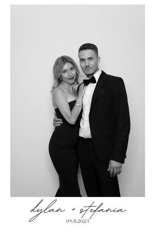 Elegant couple poses in formal black and white attire against a plain backdrop.