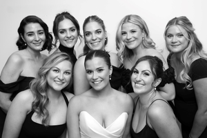 Black and white photo of bridal party wearing matching black dresses posing together and smiling at camera.