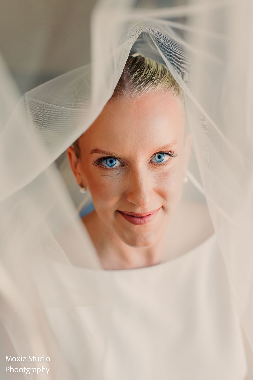 Close-up portrait of a blue-eyed bride smiling softly as a delicate sheer veil frames her face.