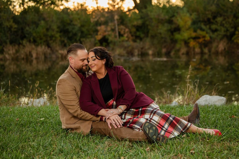 Couple sitting on grass near a pond, sharing a romantic moment at sunset in autumn.