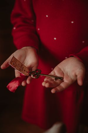 Child in a red polka dot dress holds an ornate vintage brass key with a red ribbon and paper tag in open palms.