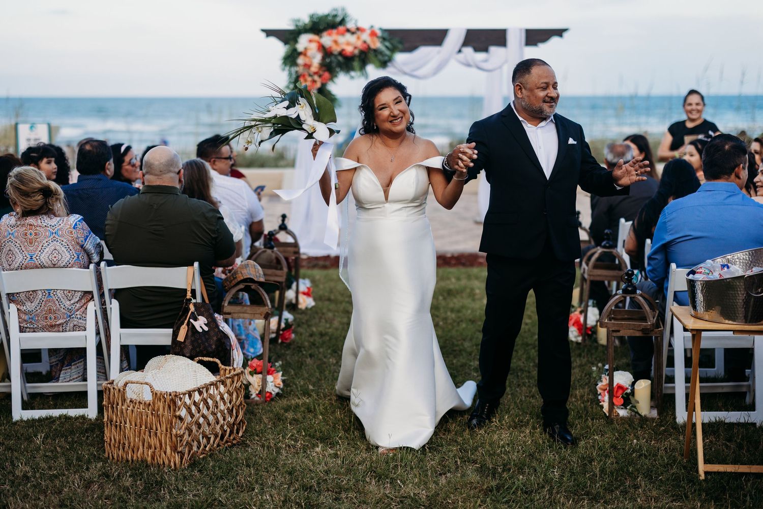 Bride and groom celebrating joyfully at an outdoor beach wedding ceremony.