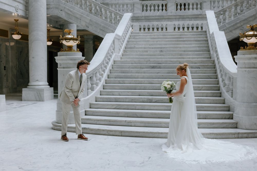 Bride and groom share a first look moment at the base of grand marble staircase in elegant venue.