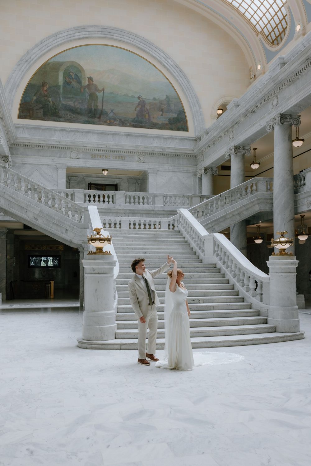 Bride and groom share joyful moment in grand marble rotunda with sweeping staircase.