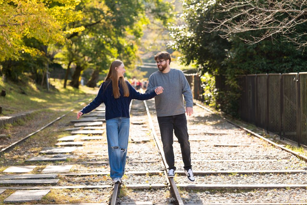 Young couple holding hands and balancing on old railway tracks while walking together through a sunny autumn park.