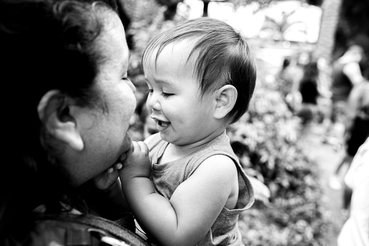 Black and white photo of a laughing baby being held by a woman outdoors.