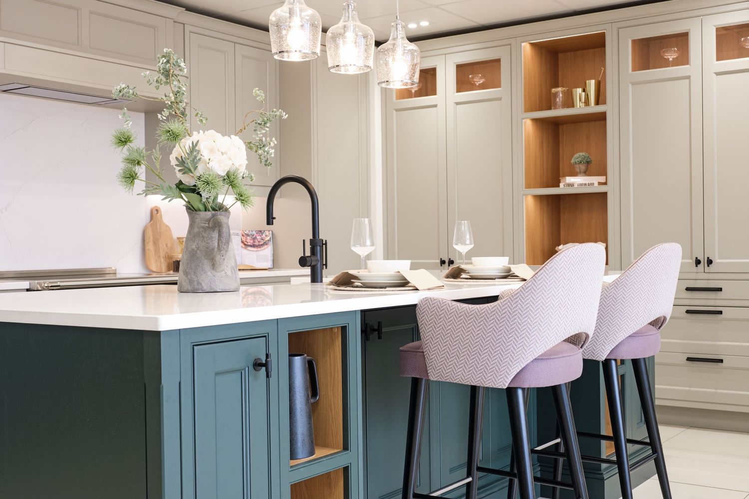 Stylish kitchen with sage green cabinetry, teal island, lavender bar stools, and elegant pendant lighting.