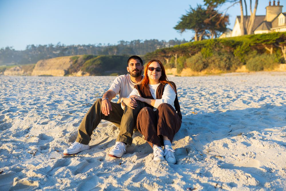 Happy couple sitting together on a white sand beach enjoying a sunny day with cliffs behind them.