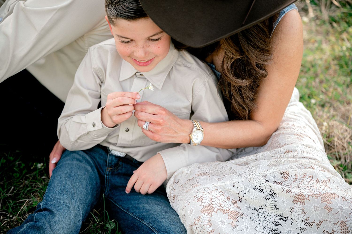 Mother and son playing with a flower while cuddled together on the ground.