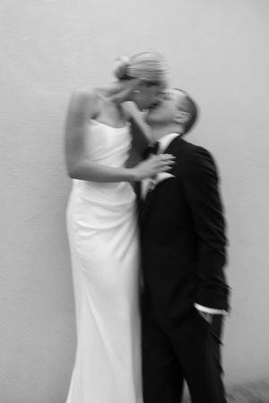 Black and white photo of a bride and groom sharing a romantic kiss, she in a white gown, he in a dark suit.