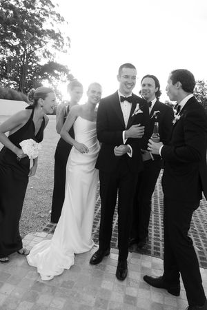 Black and white wedding party photo with bride in white gown, groom in tuxedo, bridesmaids in black dresses, and groomsmen.