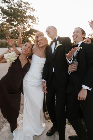 Bride, groom, and wedding party looking up and smiling at golden hour outdoor celebration.