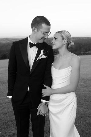 Black and white photo of a bride and groom holding hands and gazing at each other outdoors at dusk.