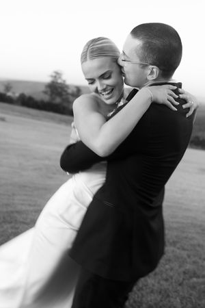 Black and white photo of a smiling bride and groom embracing outdoors on their wedding day.