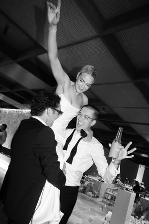 Black and white photo of a bride being lifted by groomsmen at a wedding reception celebration.
