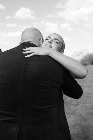 Black and white photo of a couple embracing outdoors, bride smiling with eyes closed, groom in dark suit.
