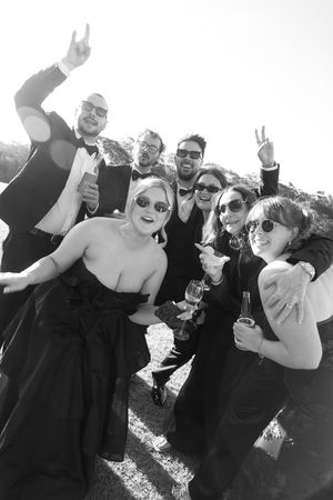 Black and white photo of a joyful group in formal attire celebrating outdoors with champagne glasses raised.