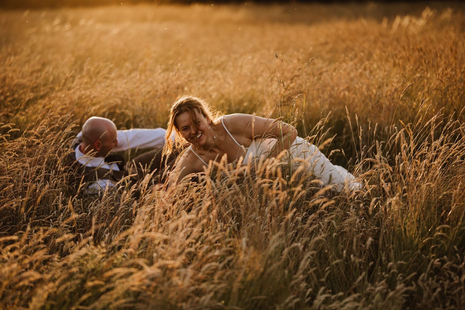 Couple lying in golden tall grass field during sunset, romantic outdoor photography.