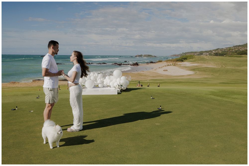 Gender reveal photoshoot at St. Regis Punta Mita, with a couple, white balloons and their dog on an oceanfront golf course.