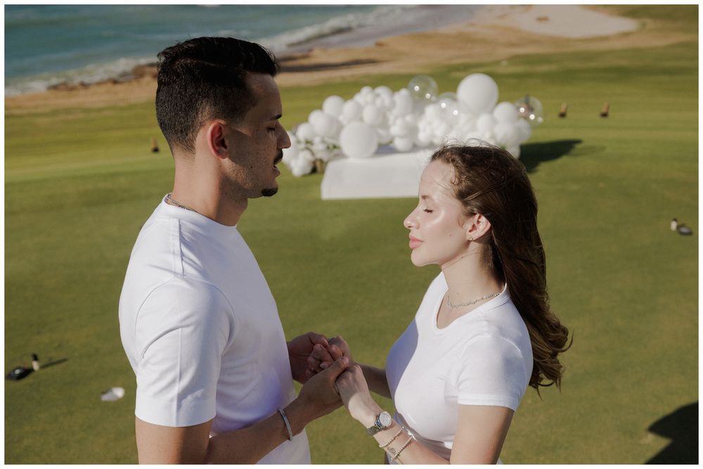 A gender reveal photoshoot at St. Regis Punta Mita, featuring a couple holding hands beneath white balloons on a green oceanfront lawn.