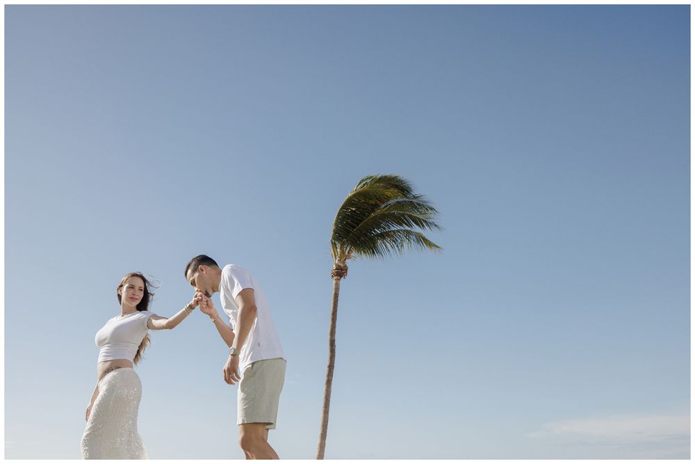 A couple dancing by the palm trees during a maternity photoshoot on the beach at Punta Mita, surrounded by ocean views and blue skies.