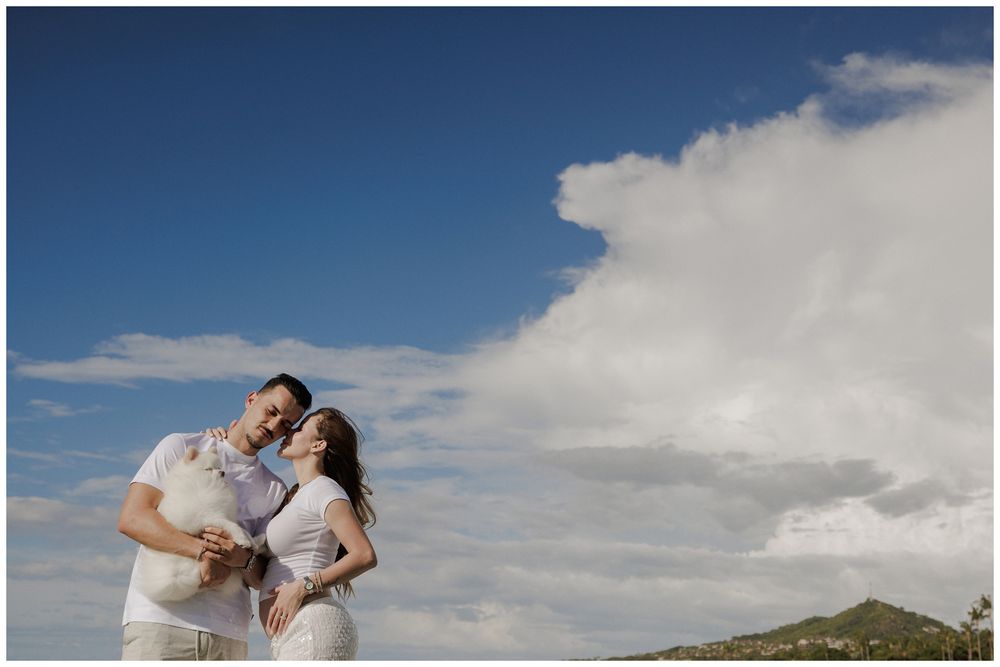 A maternity photoshoot at Punta Mita, with a couple embracing beneath dramatic clouds and green coastal hills.