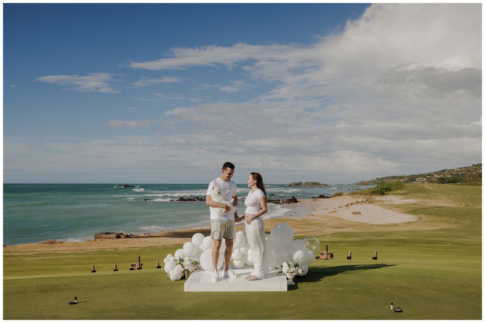 Couple standing on a white wedding altar on a lush golf course overlooking a stunning ocean coastline under blue skies.
