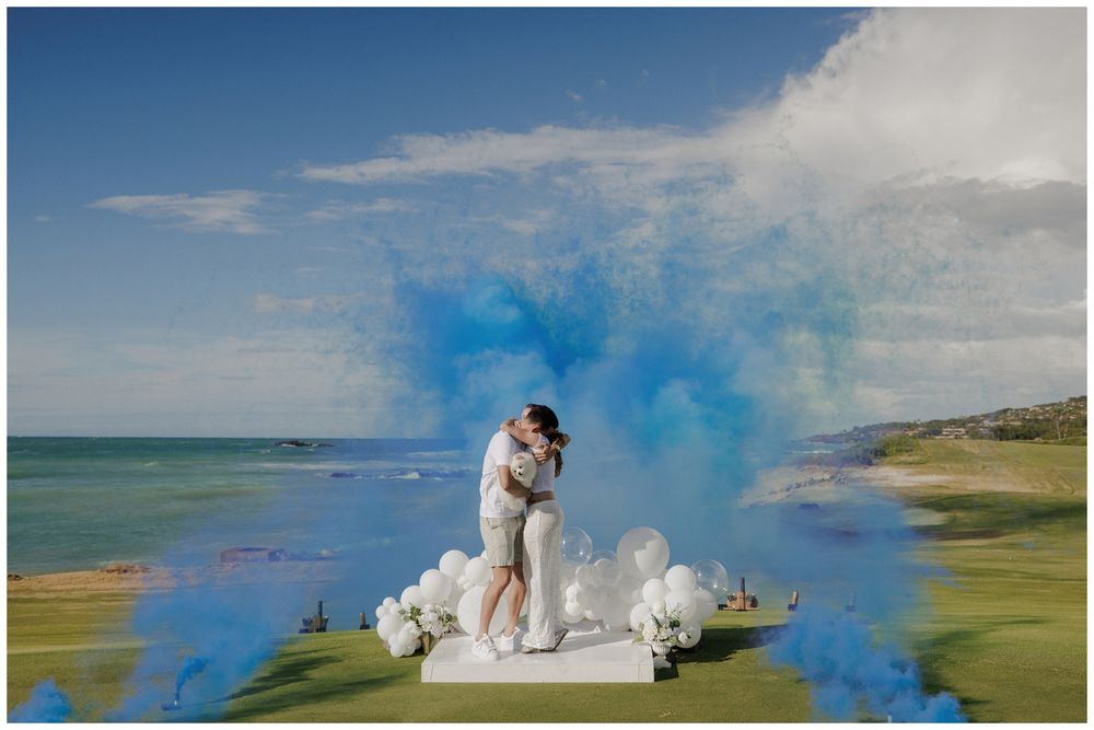 Gender reveal photoshoot at St. Regis Punta Mita, with a couple kissing amid blue smoke, white balloons, and ocean views.