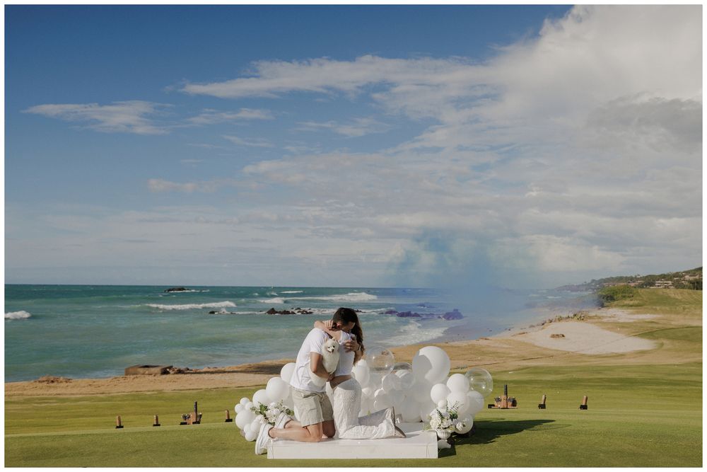 A couple shares a kiss during a beach wedding at Punta Mita, surrounded by white florals and ocean views beneath a blue sky.