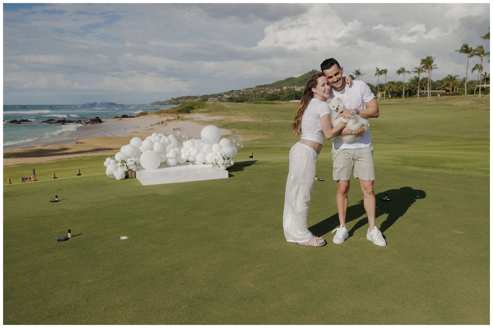 Gender reveal photoshoot at St. Regis Punta Mita, with a couple embracing beneath a white balloon arch overlooking the ocean.