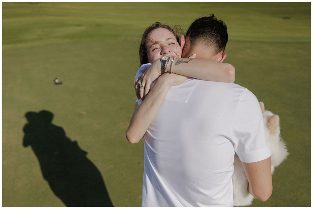 Maternity photoshoot at Punta Mita, capturing a couple embracing and laughing on a green golf course in the coastal sunlight.