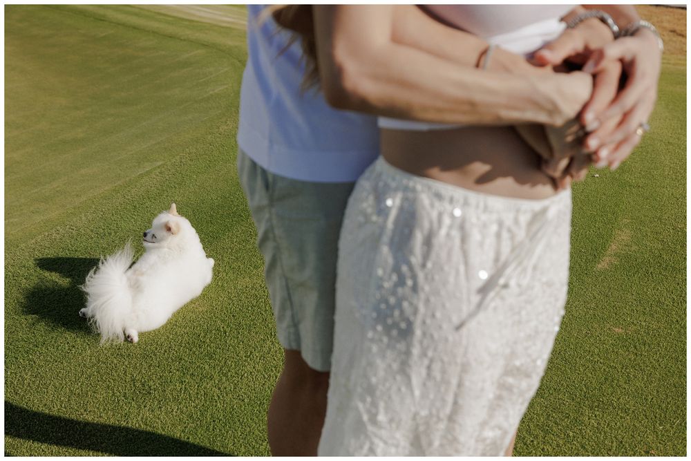 Beach family photo session at St. Regis Punta Mita, featuring a couple embracing on the green golf course with their fluffy  Pomeranian.
