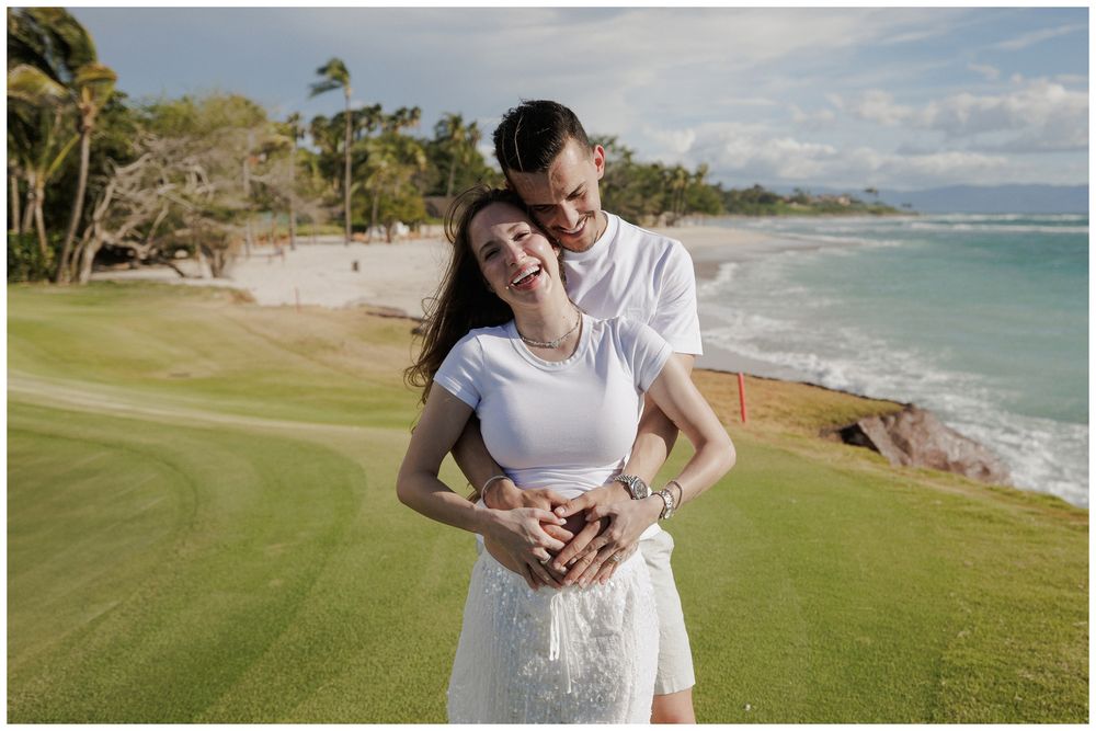 Maternity photoshoot at St. Regis Punta Mita, with a couple embracing and laughing on a lush golf course overlooking the ocean.