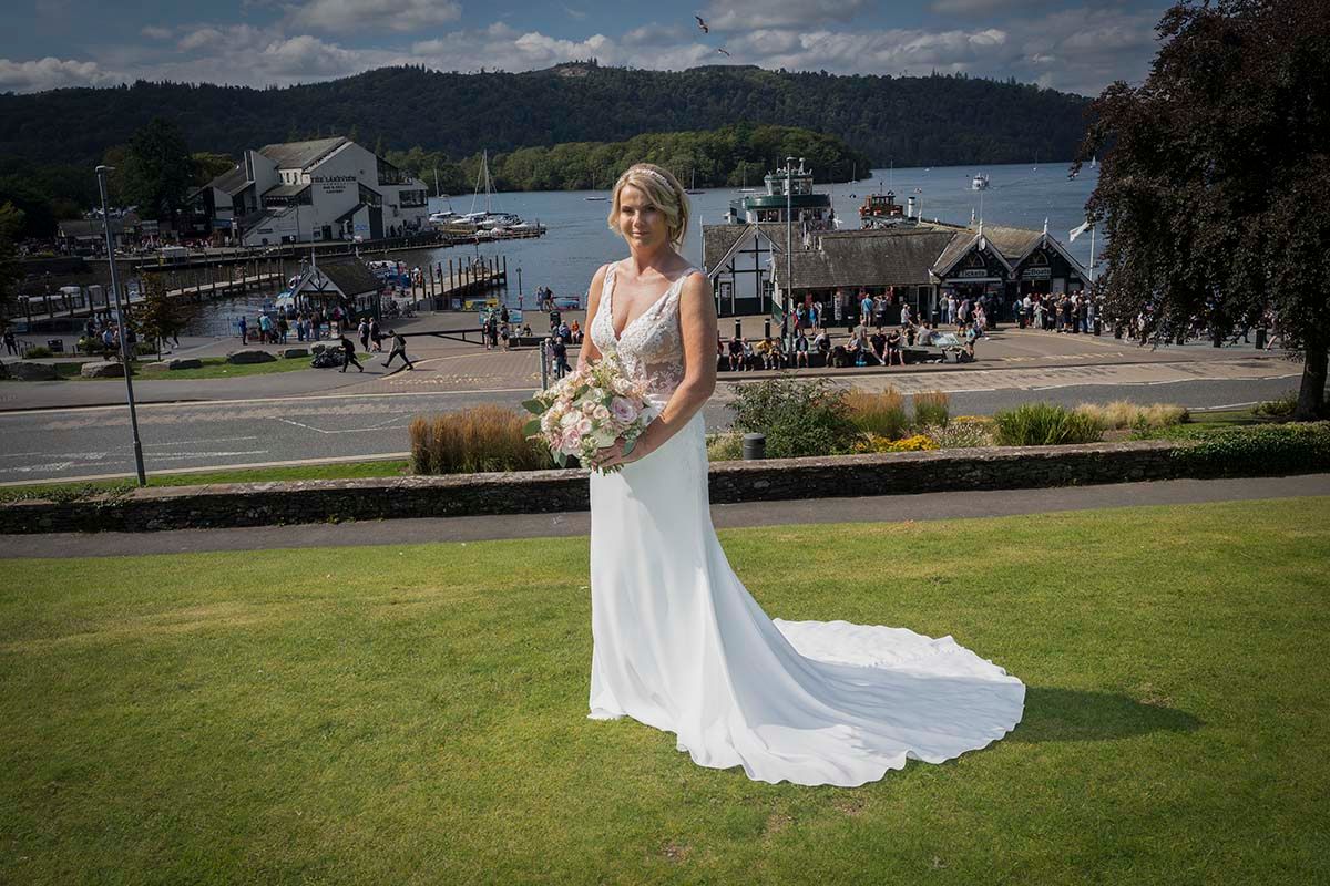 Bride holding her bouquet on the Belsfield Hotel lawn, with Lake Windermere and the surrounding hills behind her.