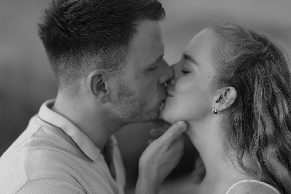 Black and white photo of a couple sharing a romantic kiss, man gently holding womans chin.