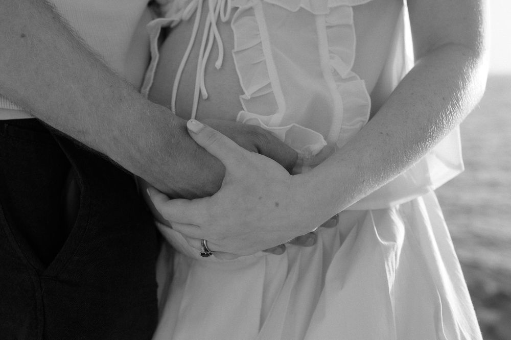 Black and white photo of a couple embracing, hands clasped together over a white dress.