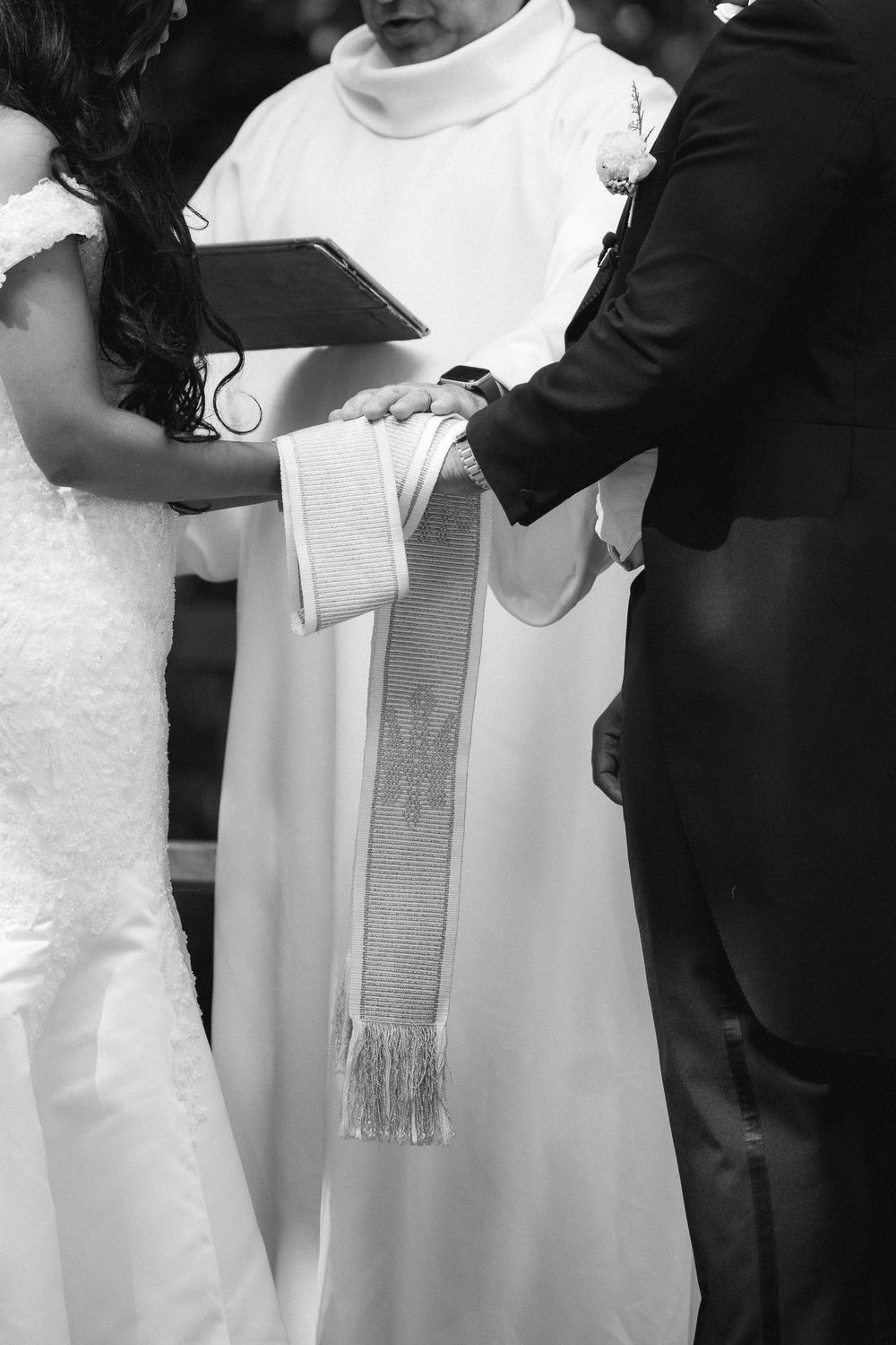Bride and groom exchange vows with officiant binding their hands in a black and white wedding ceremony photo.