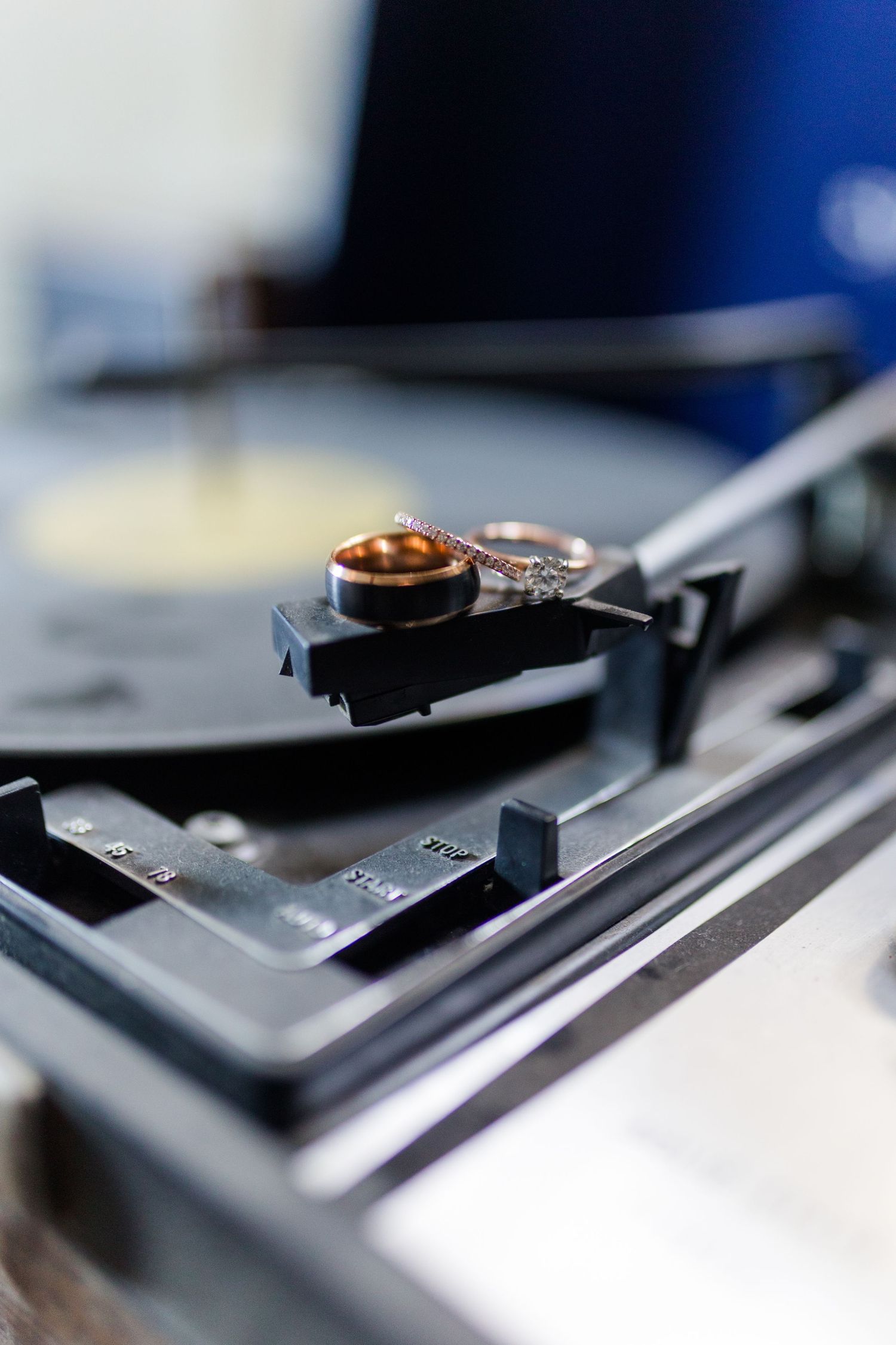 Two gold wedding rings resting on the tonearm headshell of a vintage turntable with a vinyl record spinning below.