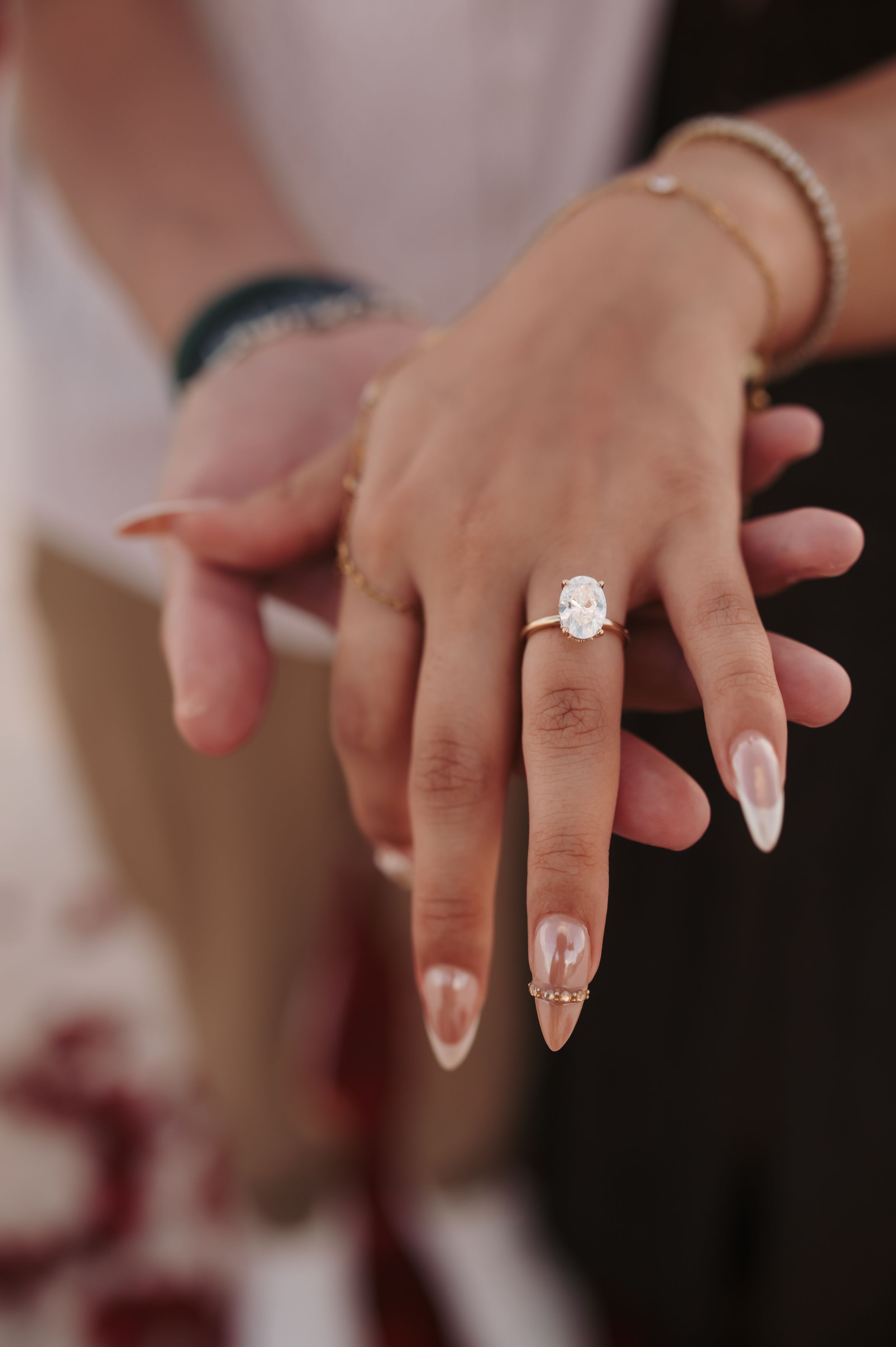 Close-up of an engagement ring with a large oval diamond on a woman's hand with nude almond-shaped nails.