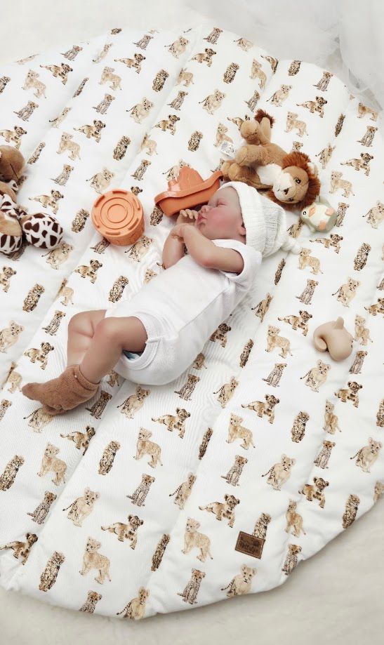 Newborn baby sleeping on a white lion print play mat surrounded by stuffed animal toys.
