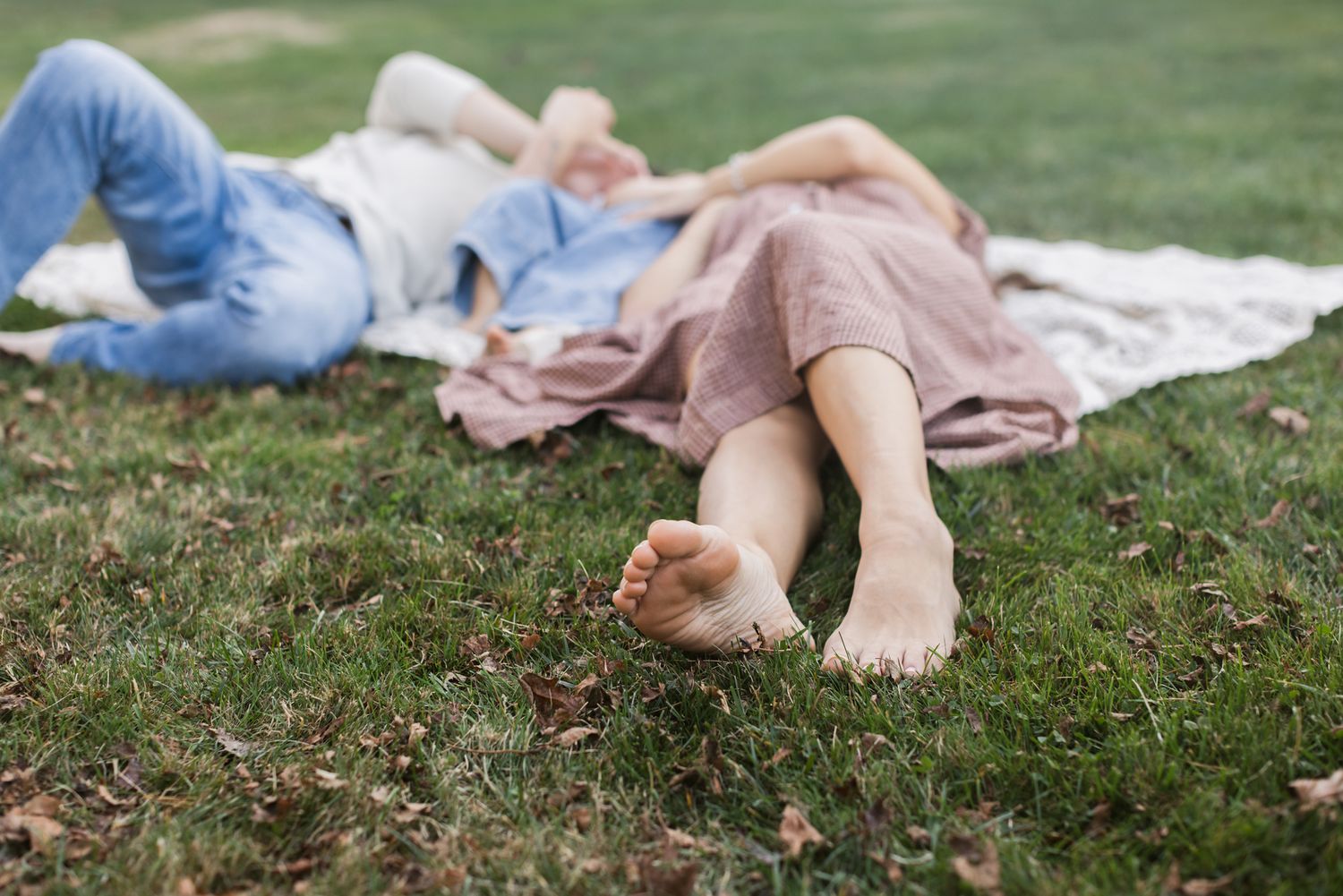 Couple lays barefoot on a crochet cream blanket in the grass with their toddler son during a fall mini shoot. Bolton family photographer.
