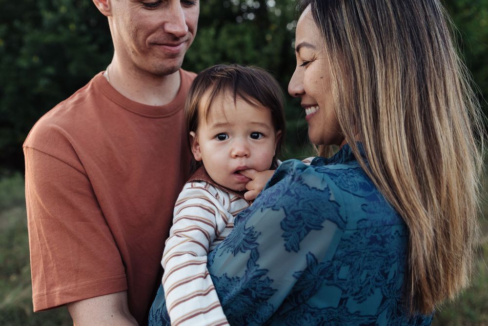 A young family with a mother and father lovingly holding their mixed-race baby outdoors.