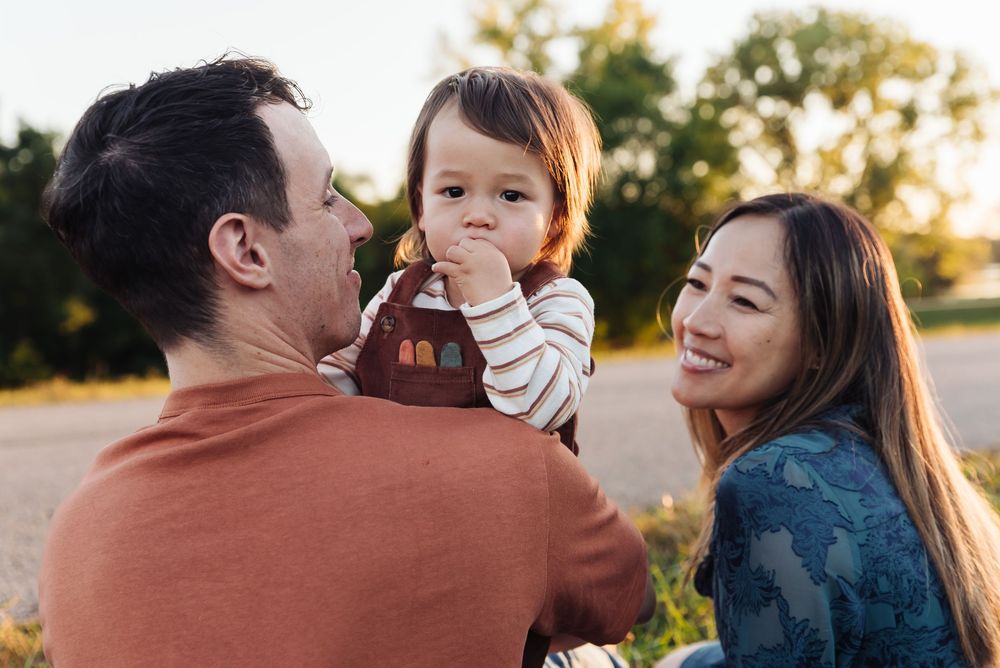 A happy family with parents smiling at their toddler outdoors during golden hour.