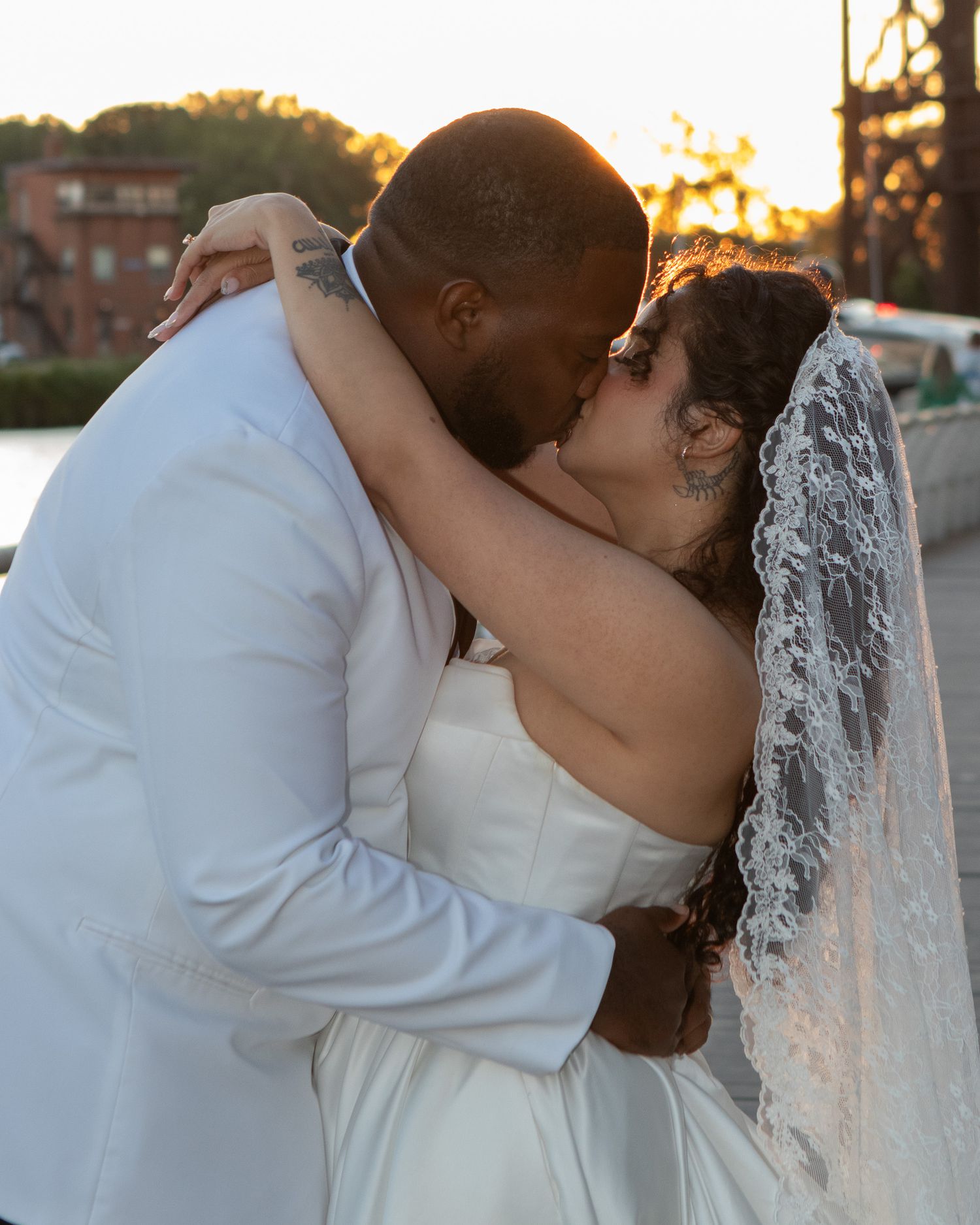 A bride and groom share a romantic sunset kiss outdoors on their wedding day.