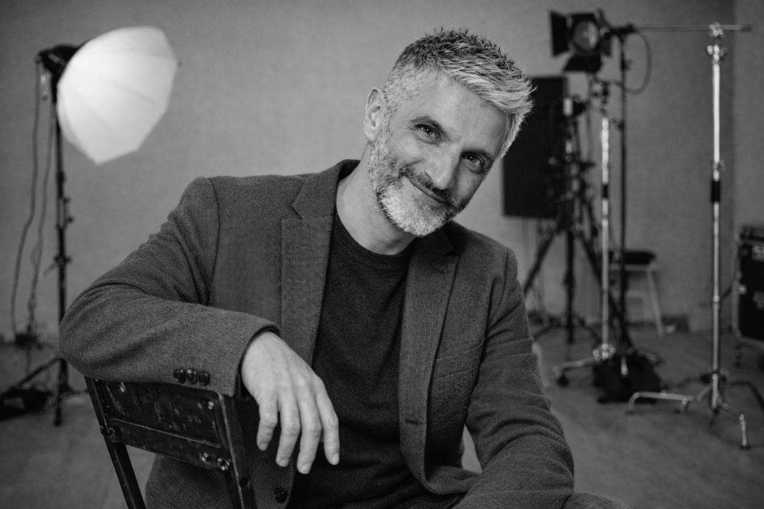 Smiling gray-haired bearded man in blazer posing in black and white studio portrait.