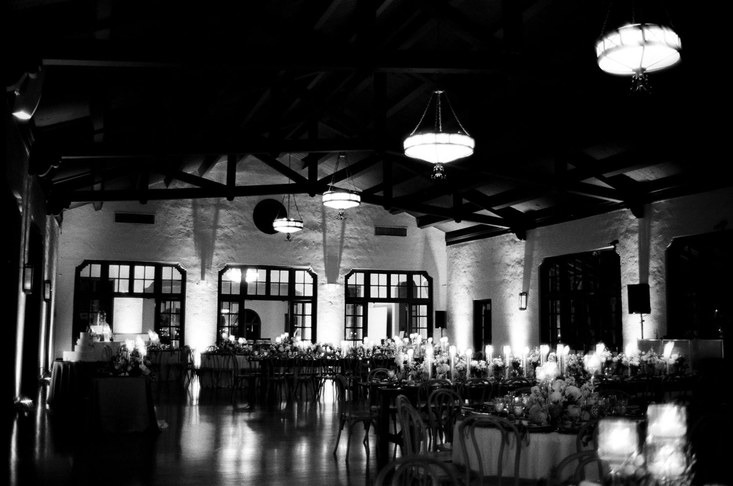 Elegant black and white banquet hall with chandeliers, arched windows, and candlelit reception tables.